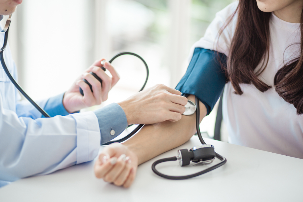 Doctor checking female patient's blood pressure.