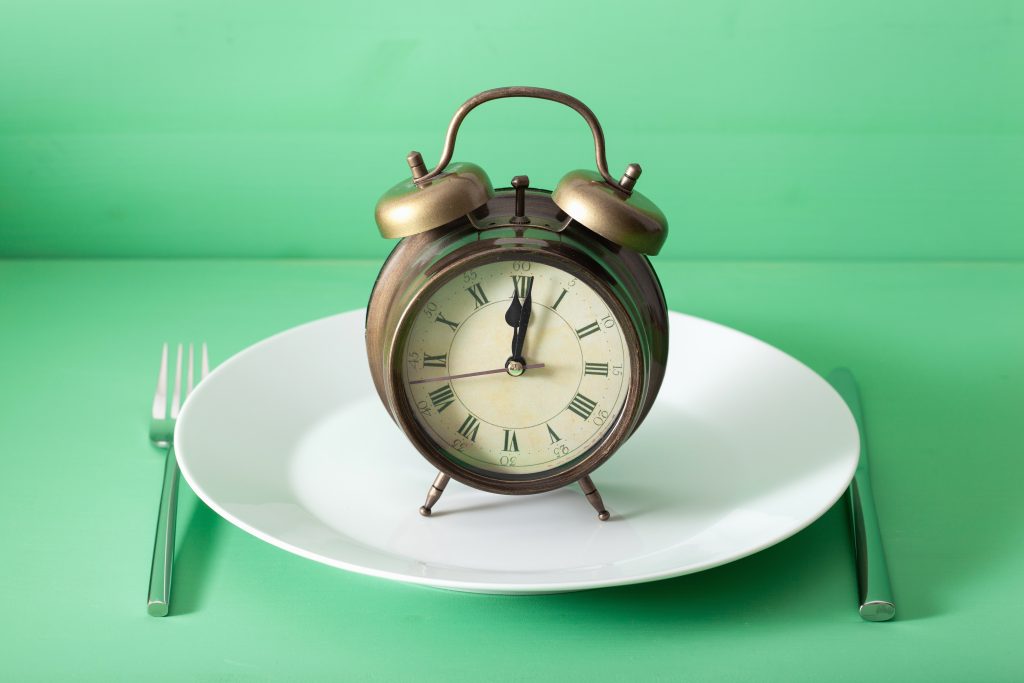 concept of intermittent fasting, ketogenic diet, weight loss. alarmclock on a plate