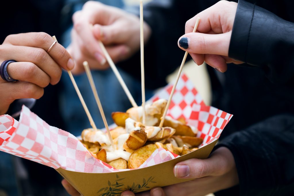 Close-up of group of friends visiting eat market and eating potatoes in the street.