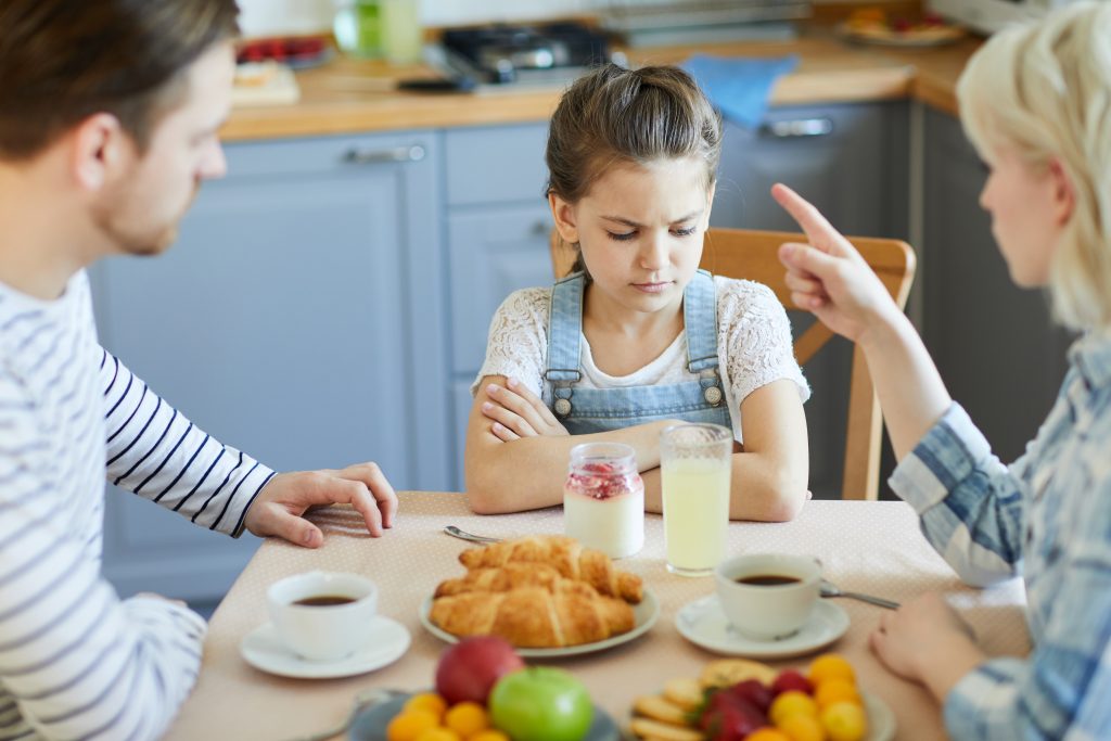Sad little girl sitting by table while mother forbidding her to have dessert because of bad behavior