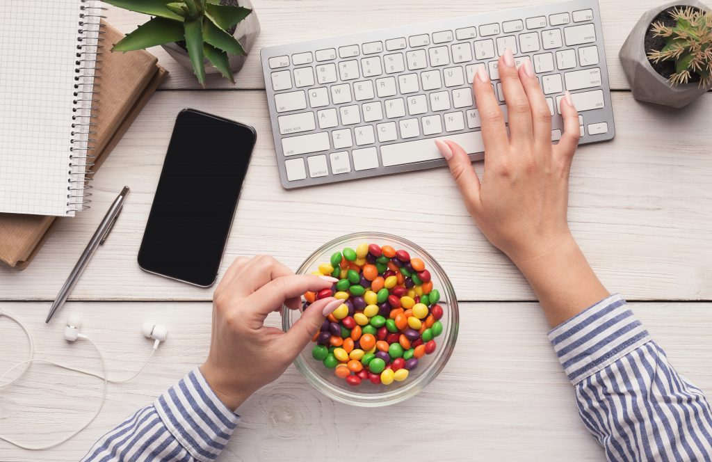 Bad habit. Work space with laptop, candies and woman hands on white background, top view