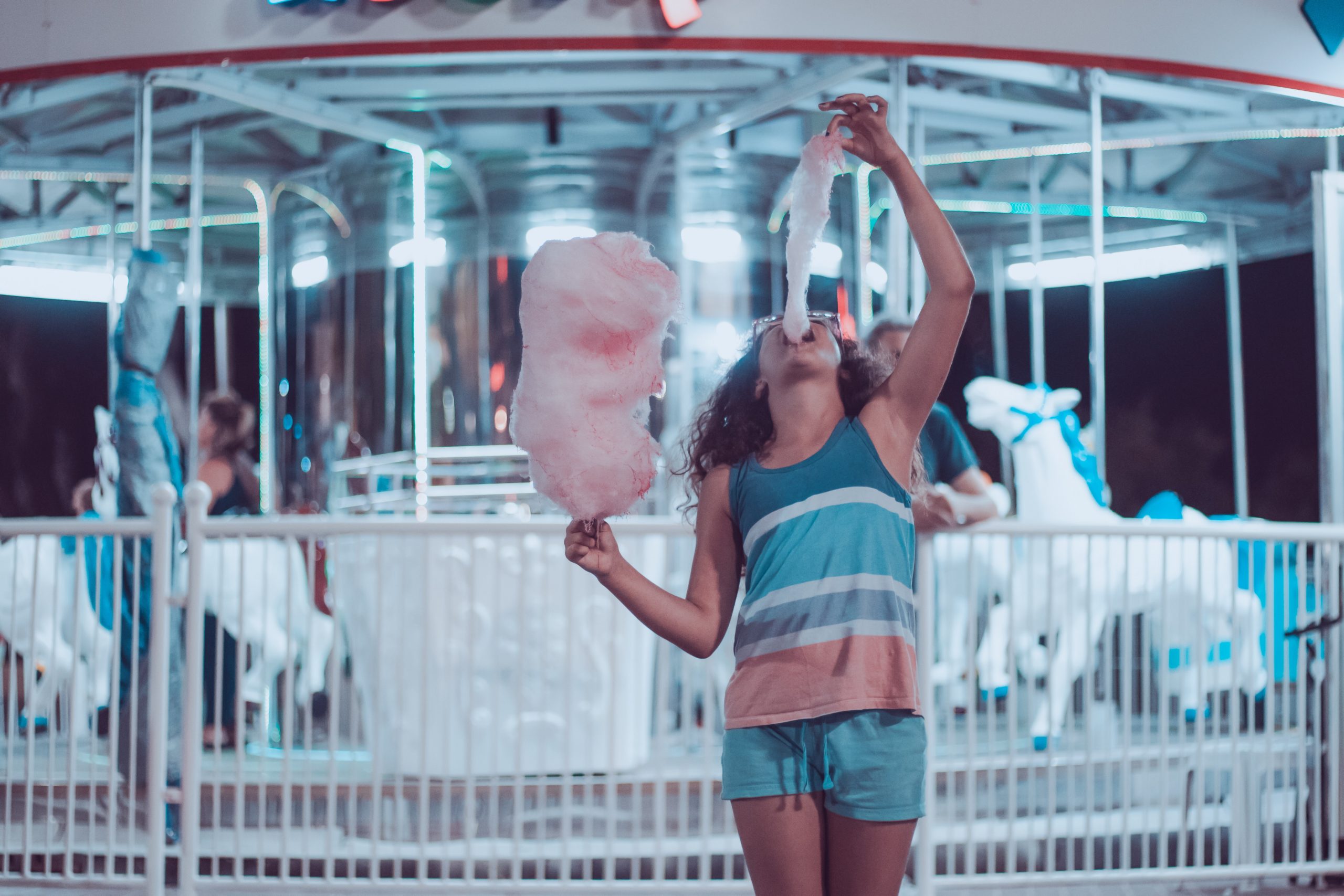 Woman eating cotton candy in front of carousel.