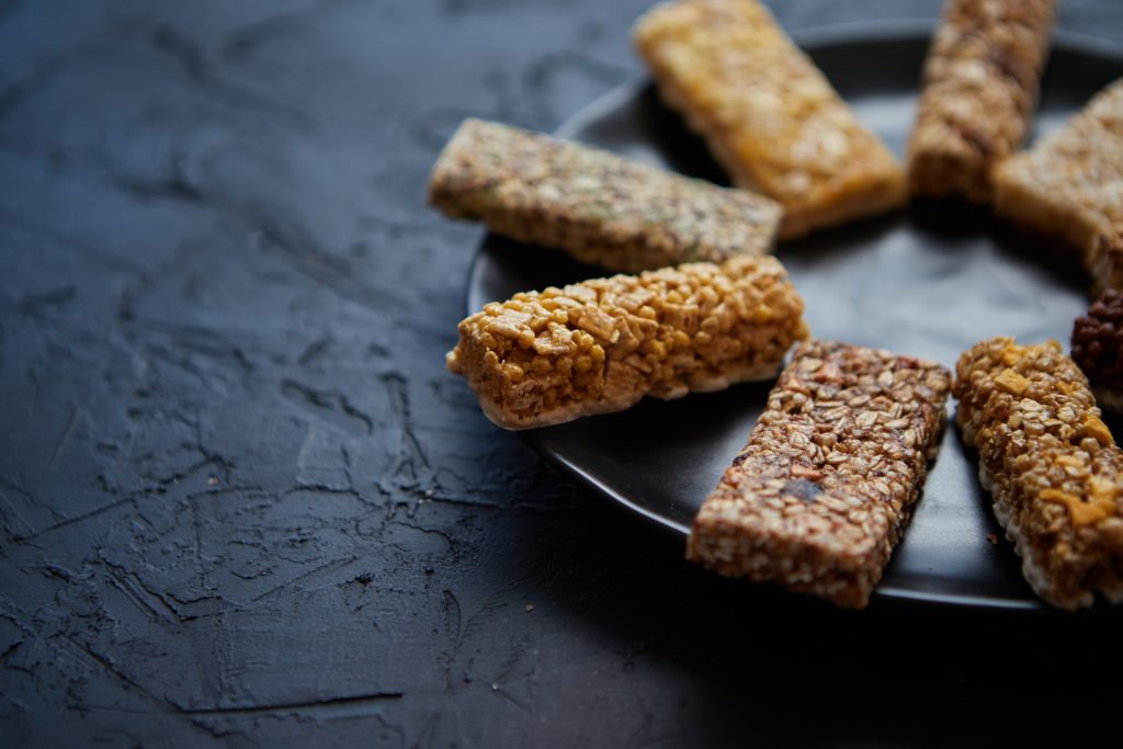 Different kind of granola fitness bars placed on black ceramic plate on a table. Healthy diet concept. Top view with copy space.
