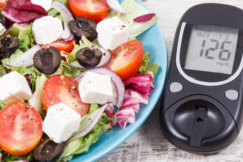 Glucose meter and fresh prepared greek salad with feta cheese and vegetables. Best healthy food for diabetics, dieting and slimming