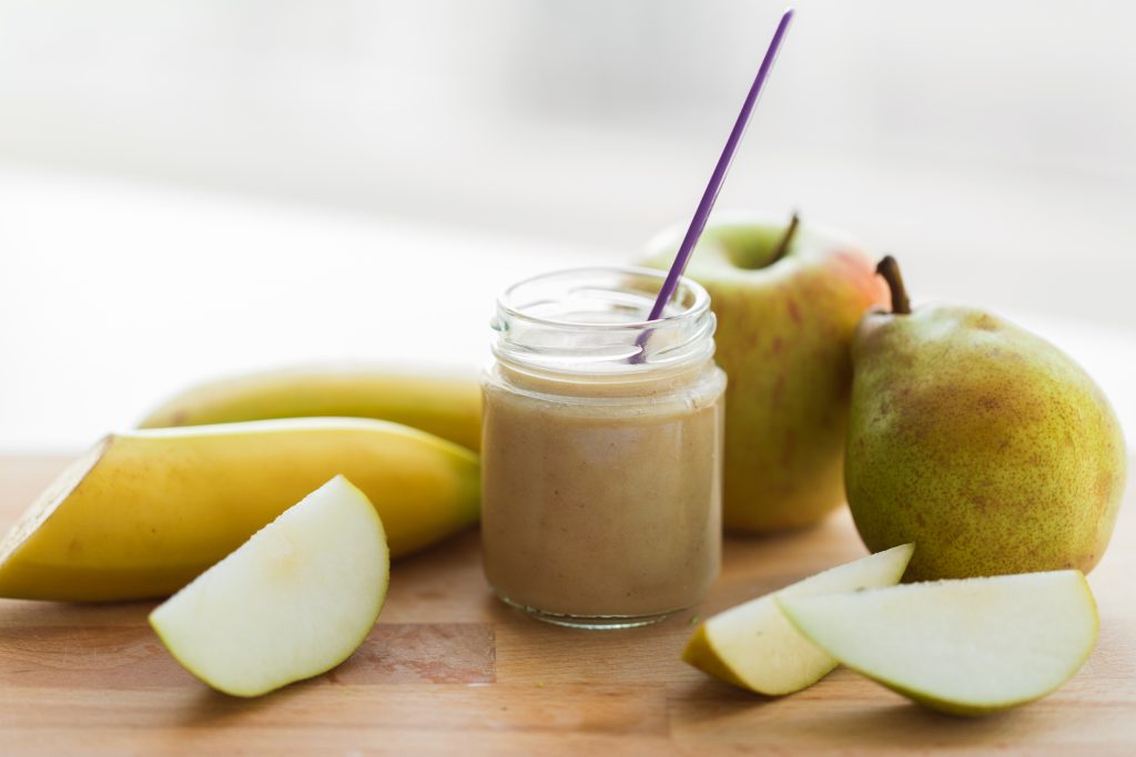 baby food, healthy eating and nutrition concept - glass jar with apple, pear and banana fruit puree on wooden board