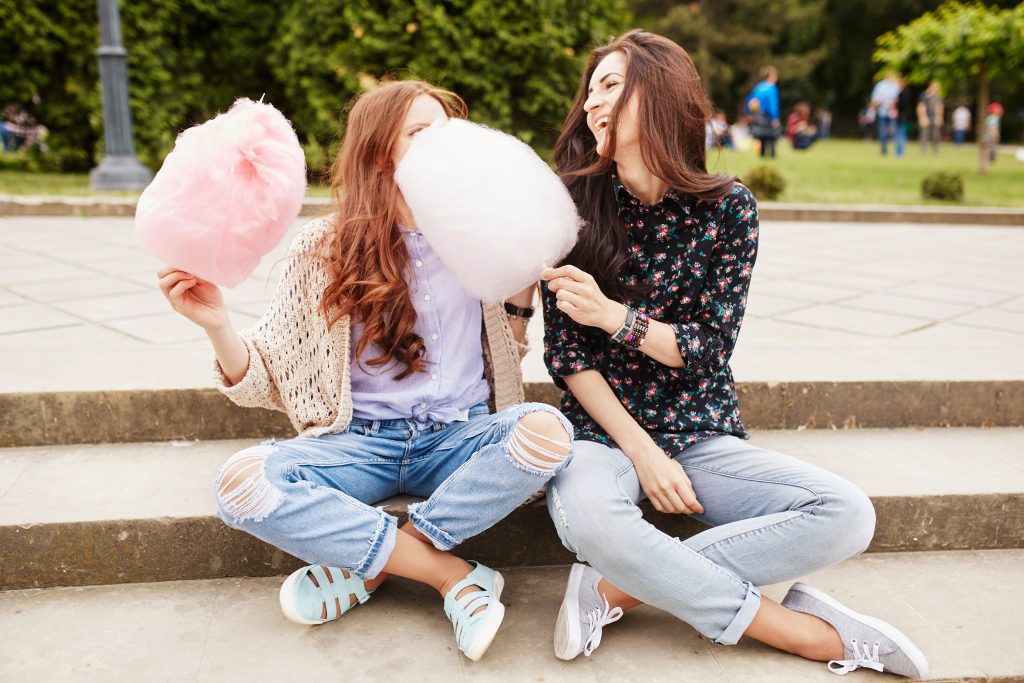 Two cheerful sisters eating cotton candy at the park