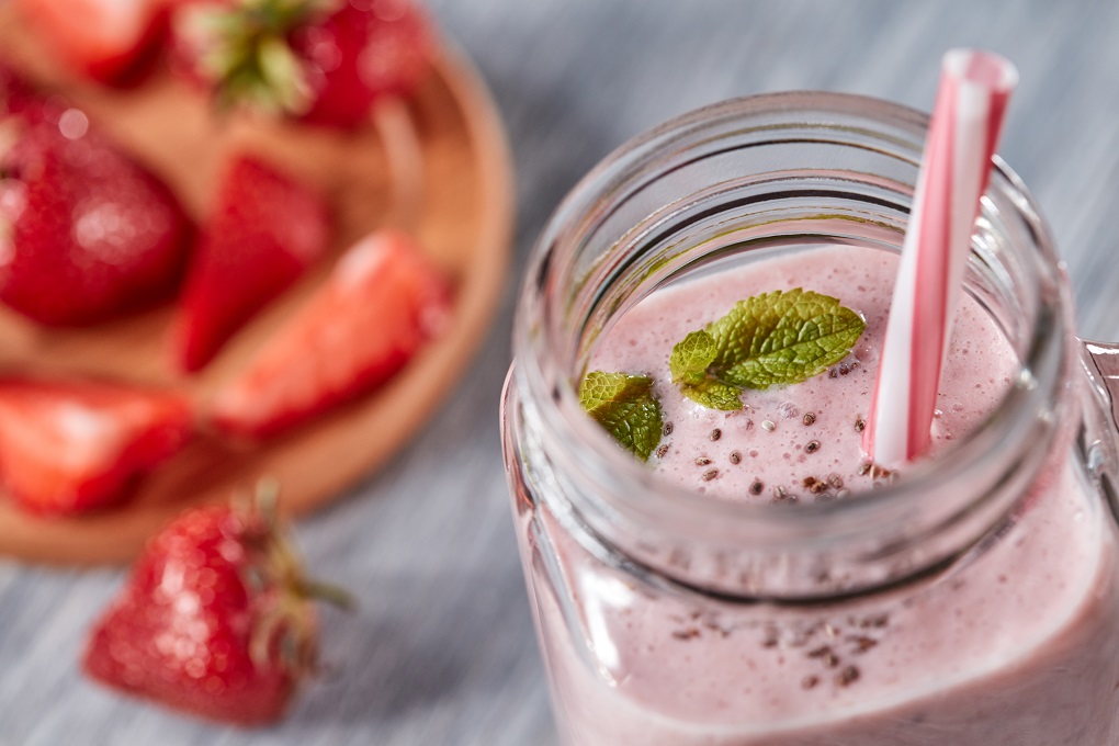 Closeup of homemade strawberry milk shake with chia seeds and green mint leaves in a jar with a tubule on a wooden background. Organic vitamin dessert. Top view
