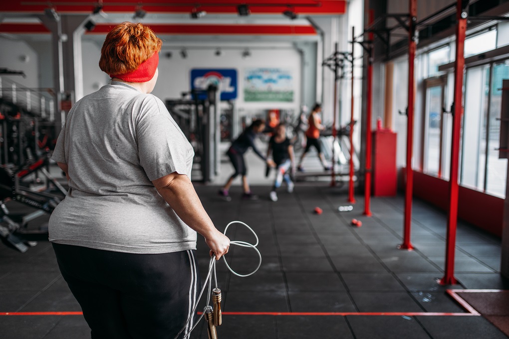 Fat sweaty woman, fit training with rope in gym. 