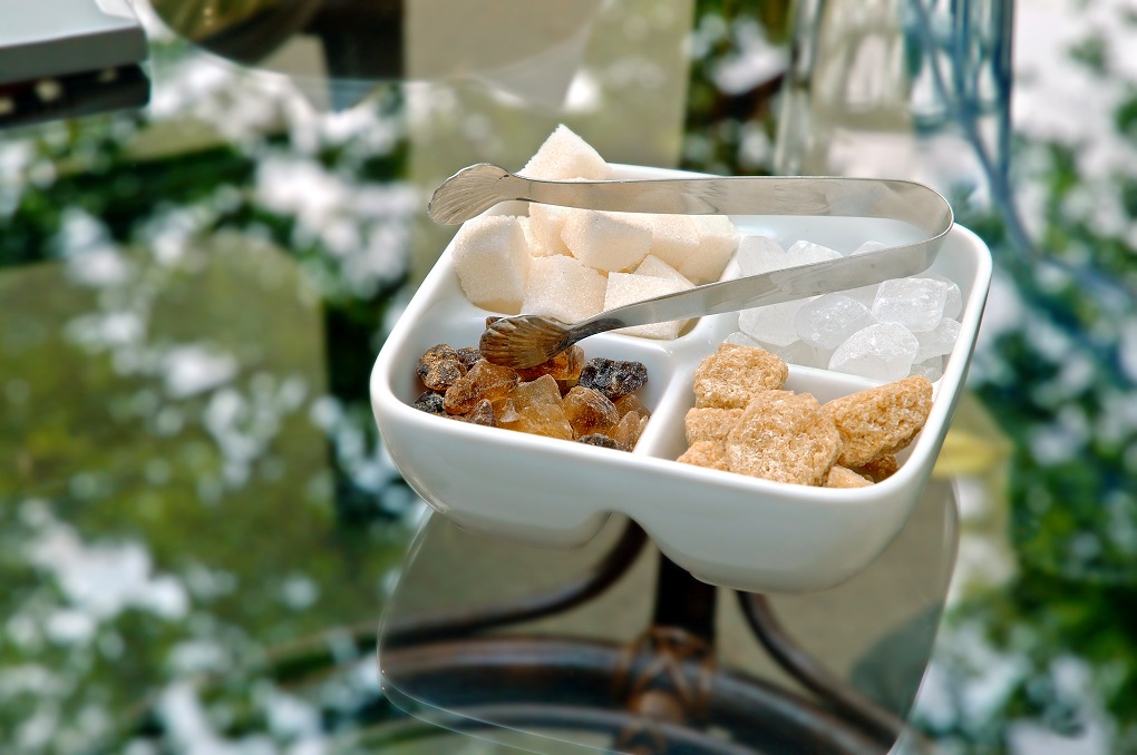 Ceramic sugar bowl with white and brown cubes of grape-sugar, cane-sugar, fruit sugar and lump sugar on glass table in open-air cafe.