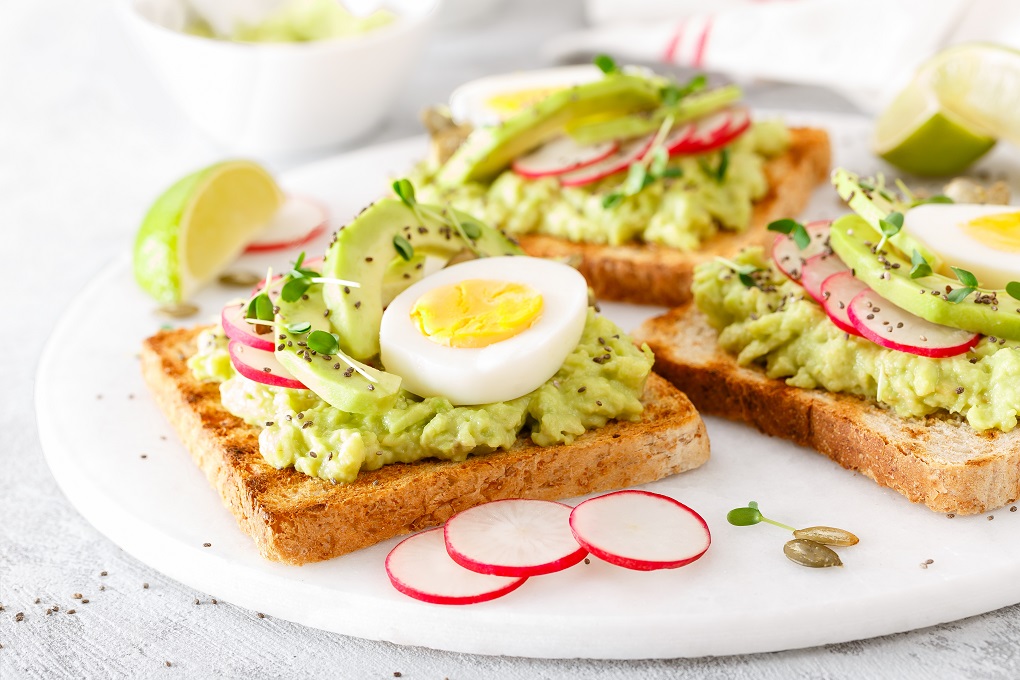 Toasts with avocado guacamole, fresh radish, boiled egg, chia and pumpkin seeds. Diet breakfast. Delicious and healthy plant-based food. Closeup