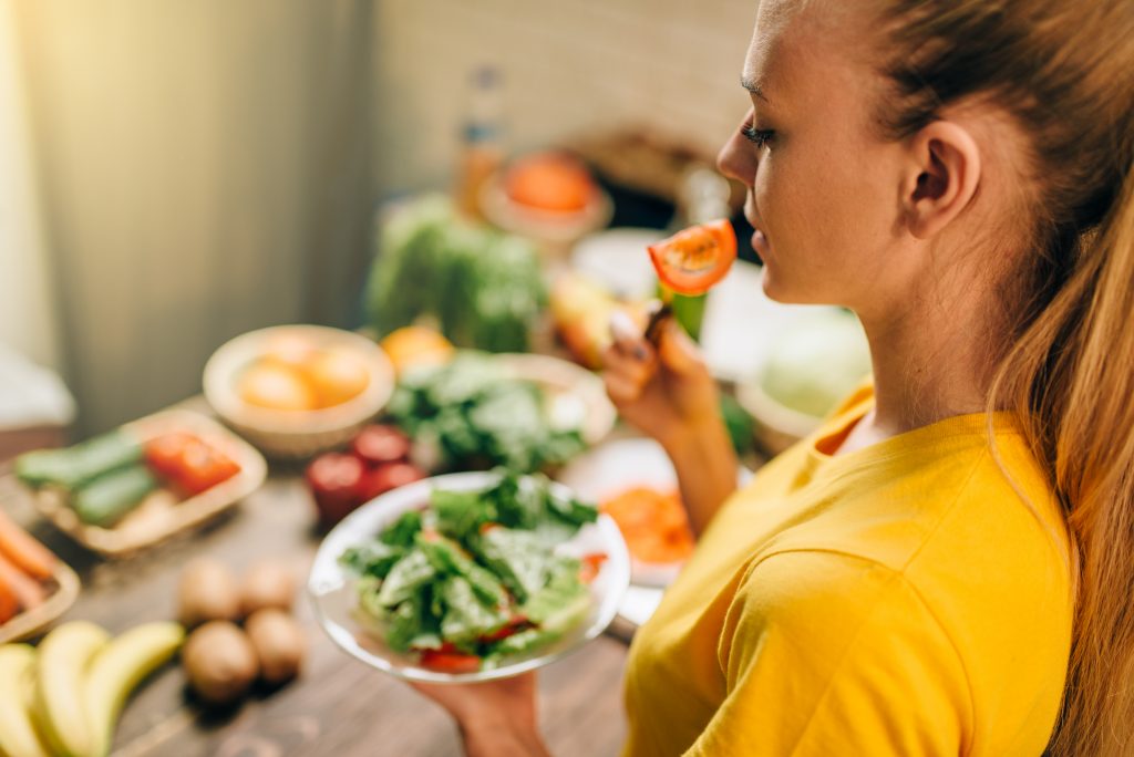 Young woman eating on the kitchen, healthy eco food. Vegetarian diet, fresh vegetables and fruits