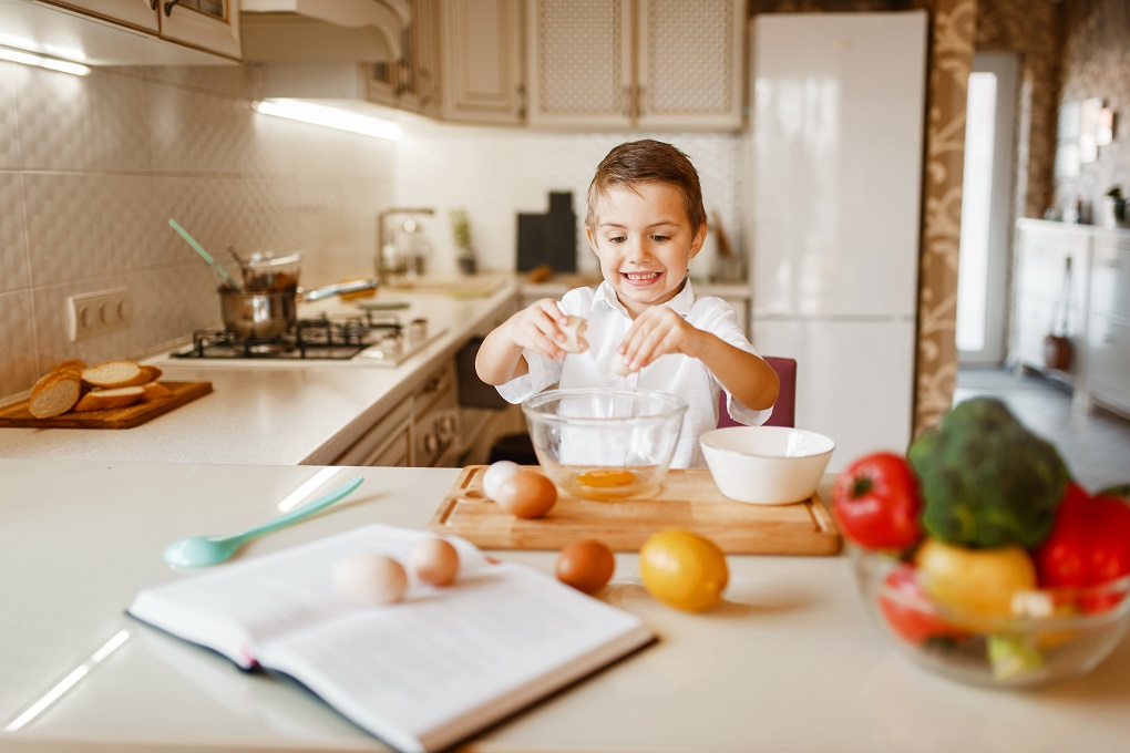 Litte boy stirs raw eggs in a bowl, pastry preparation. Kid cooking on the kitchen. Happy child prepares sweet dessert