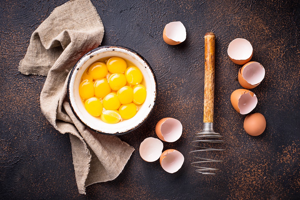 Bowl with eggs yolks and vintage whisk. Top view