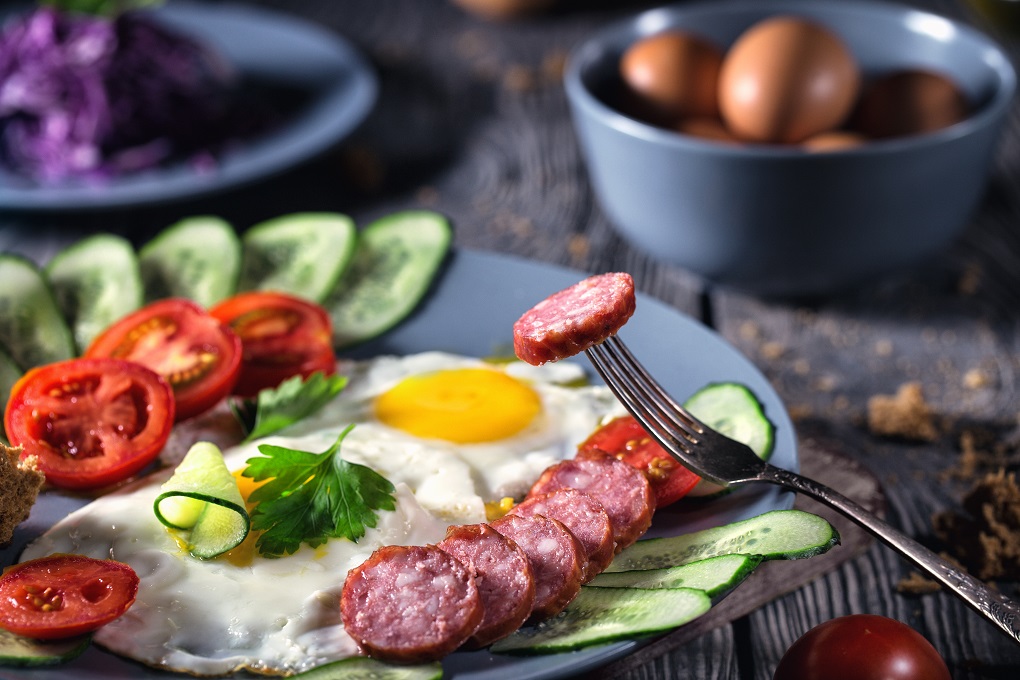 Fried eggs with vegetables and sausage on table. The concept of healthy food. Breakfast in rustic style.