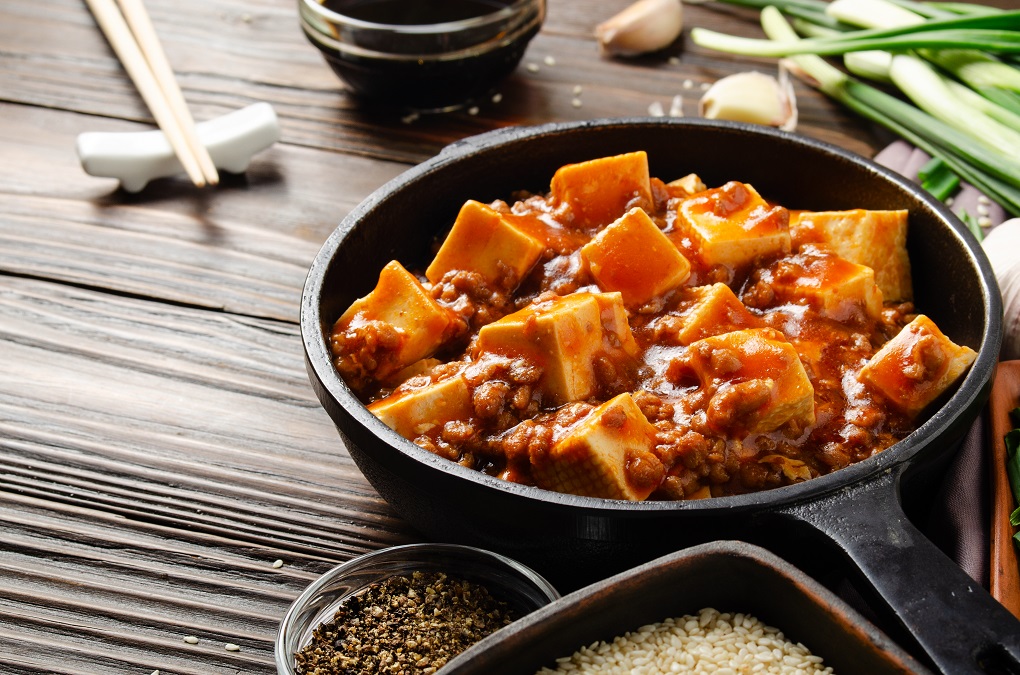 Traditional Chinese food mapo tofu in cast iron skillet with pork chives soy sauce sichuan pepper garlic and spices closeup on wooden table
