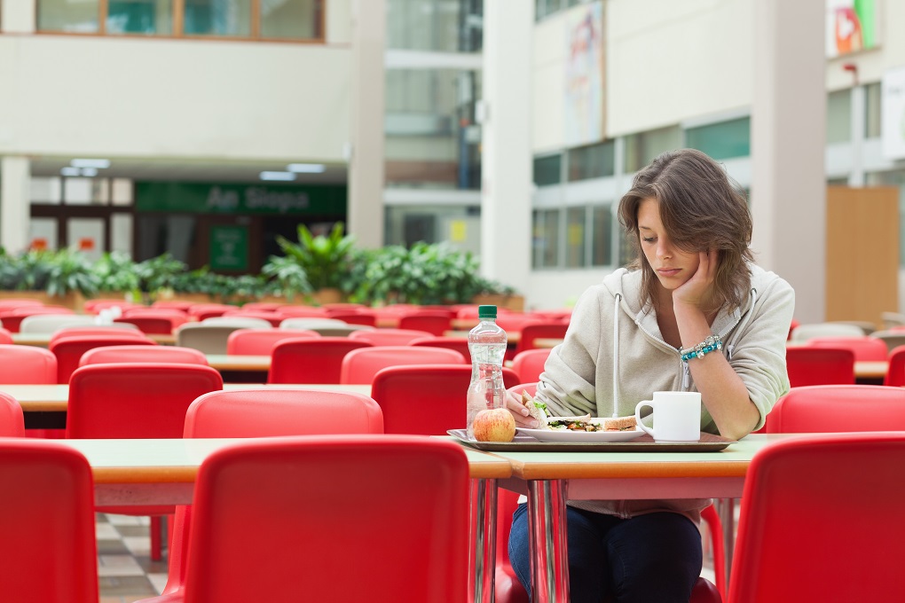 Alone and sad female student sitting in the cafeteria with food tray
